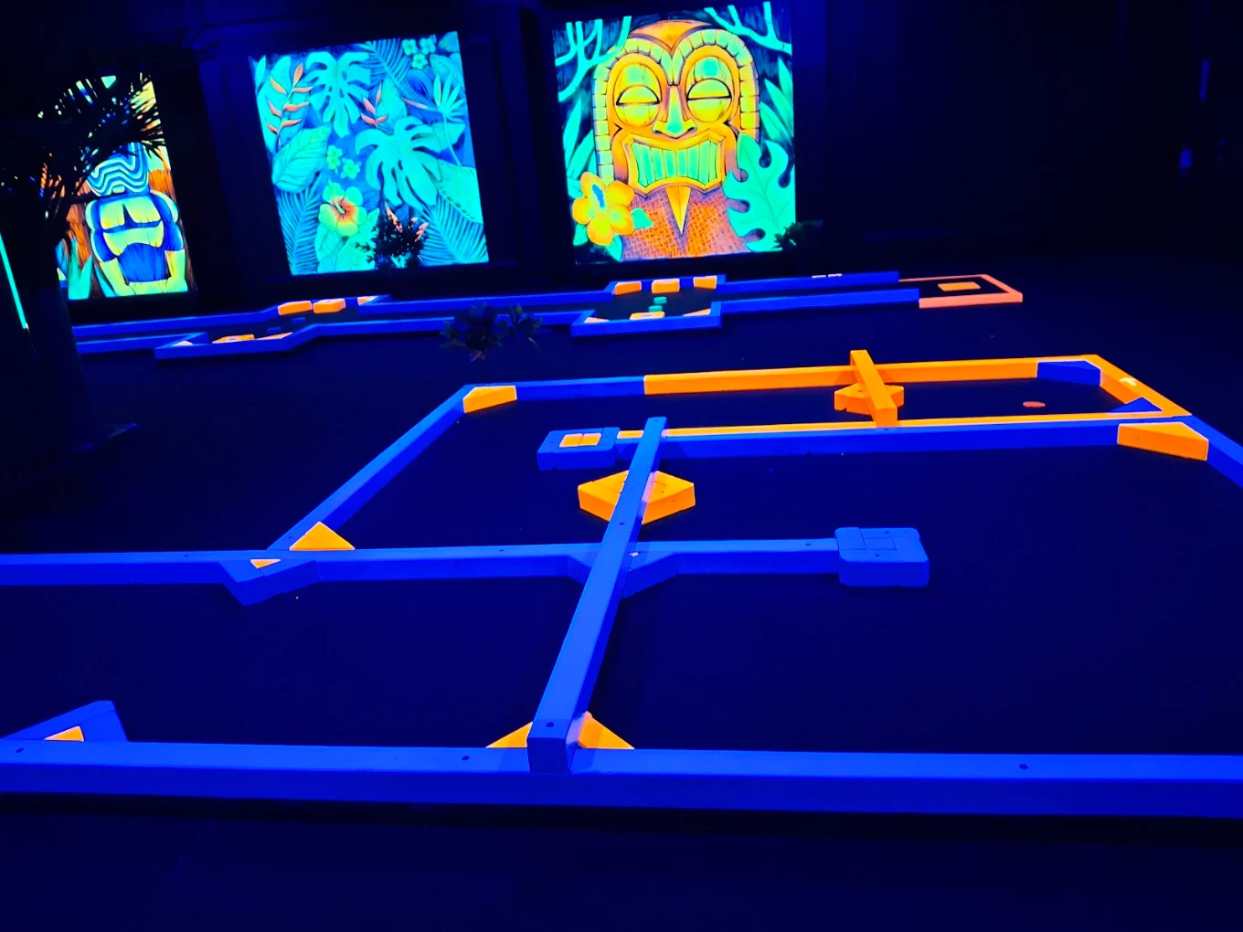 Overview of glowing mini golf lanes beneath tiki and jungle murals