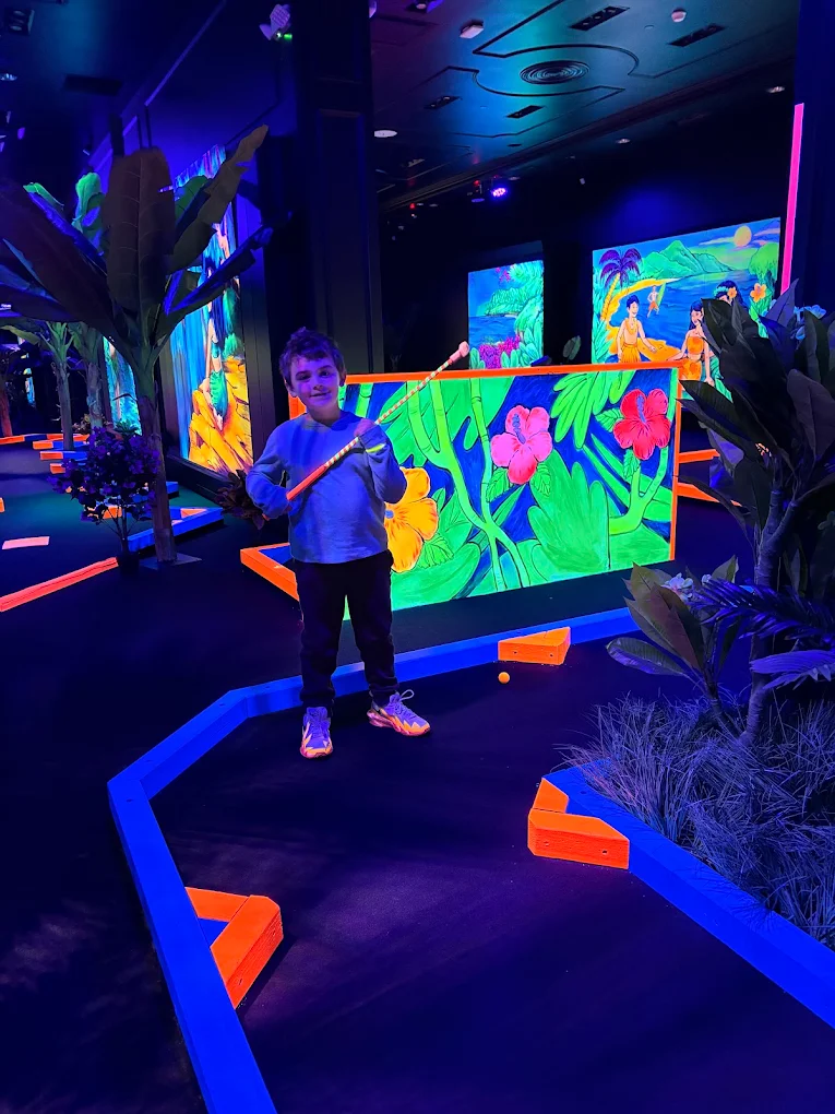 Young player holding a putter in front of a hibiscus jungle mural