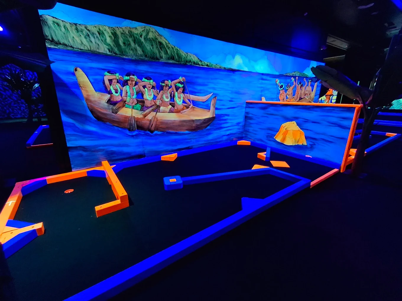 Glowing Hawaiian outrigger canoe mural above a blacklight mini golf fairway