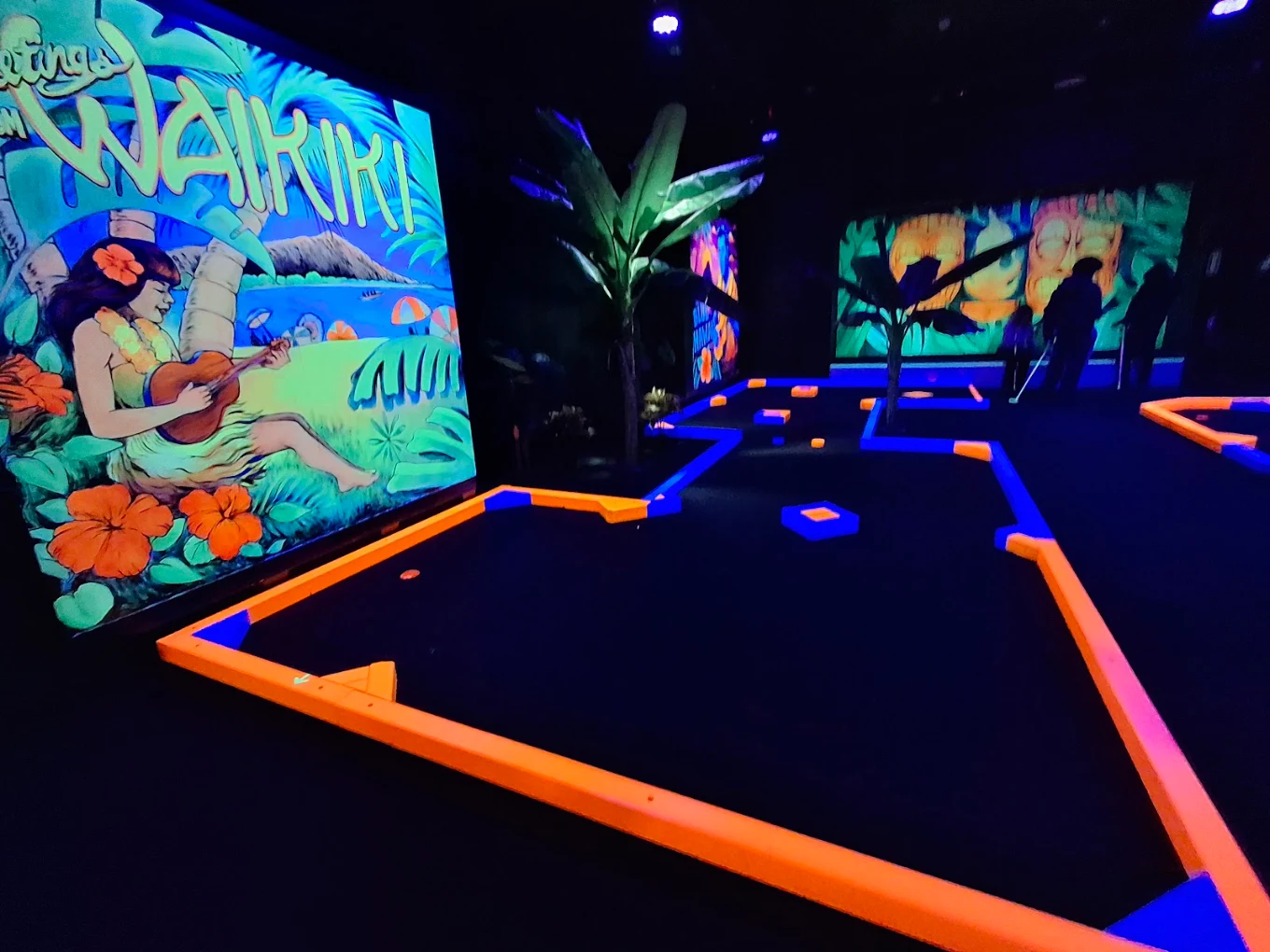 Greetings from Waikiki mural running along a neon-outlined mini golf hole